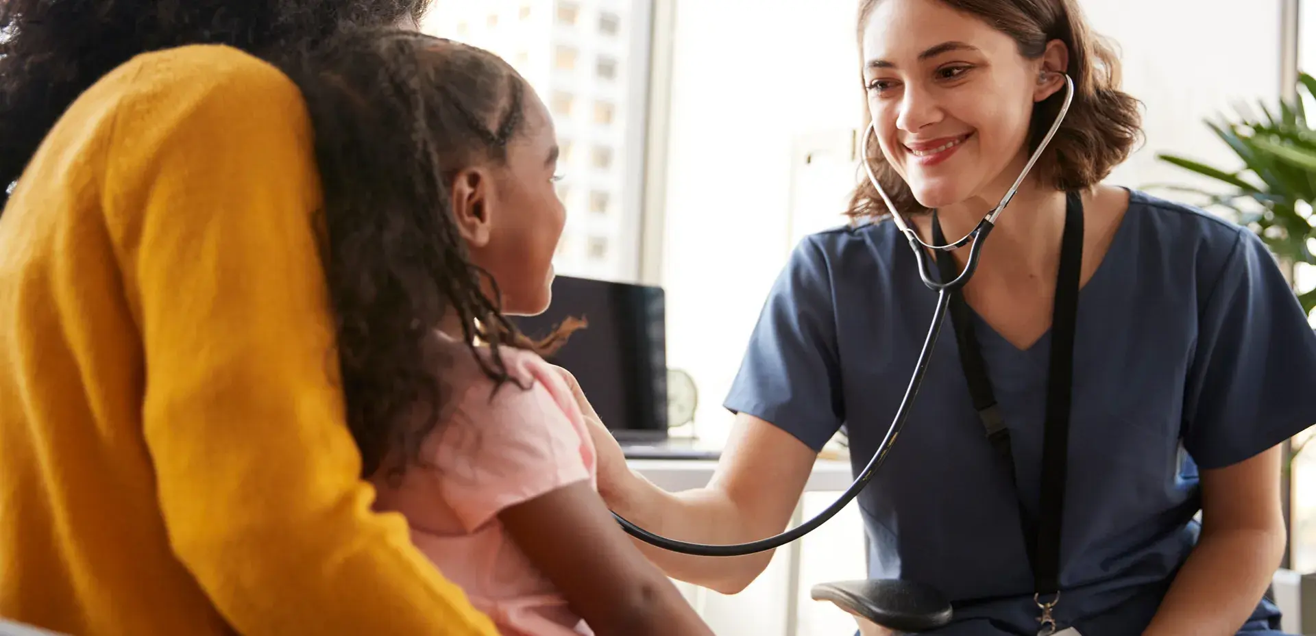 Nurse checking on a child who is sitting on their mother’s lap