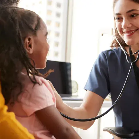 Nurse checking on a child who is sitting on their mother’s lap